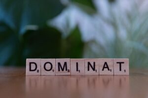 Scrabble tiles spelling 'DOMINAT' on a wooden surface with blurred background.